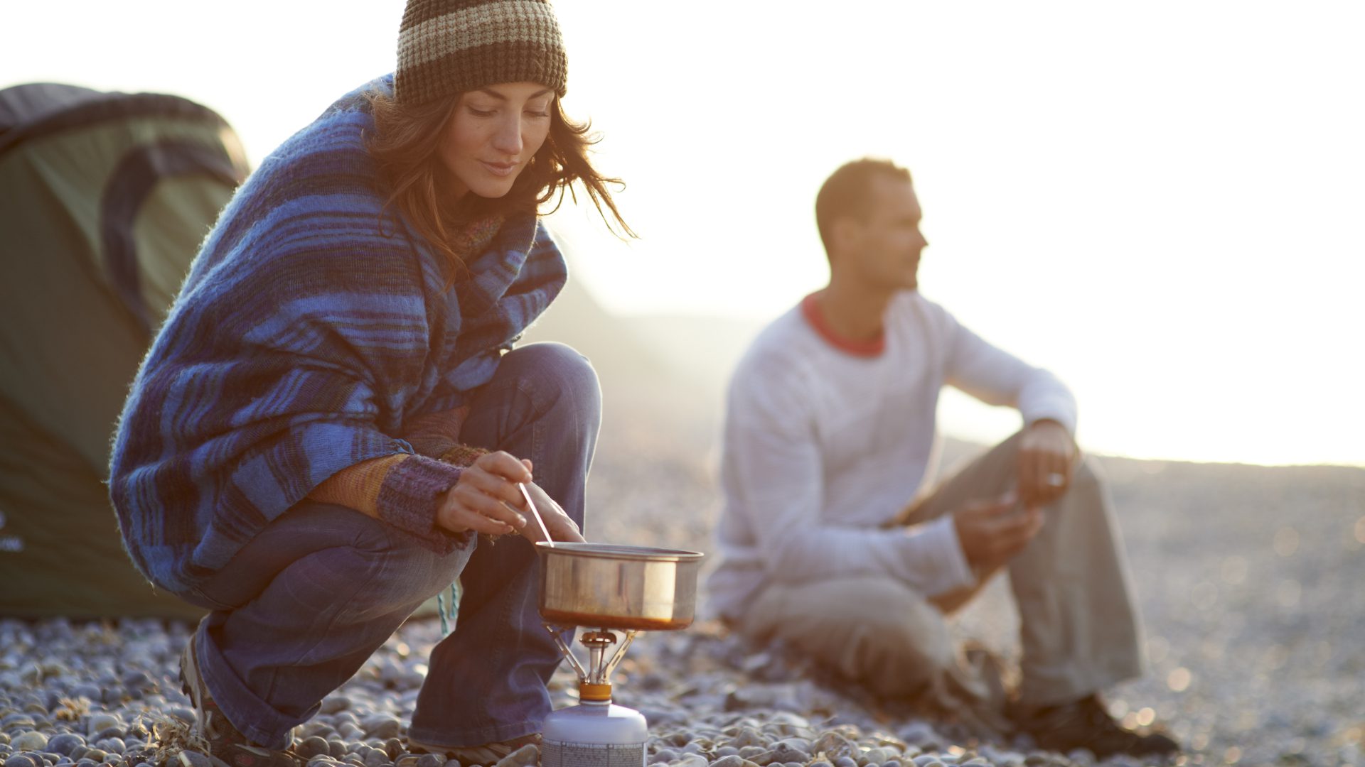 Woman cooking outside tent on beach.